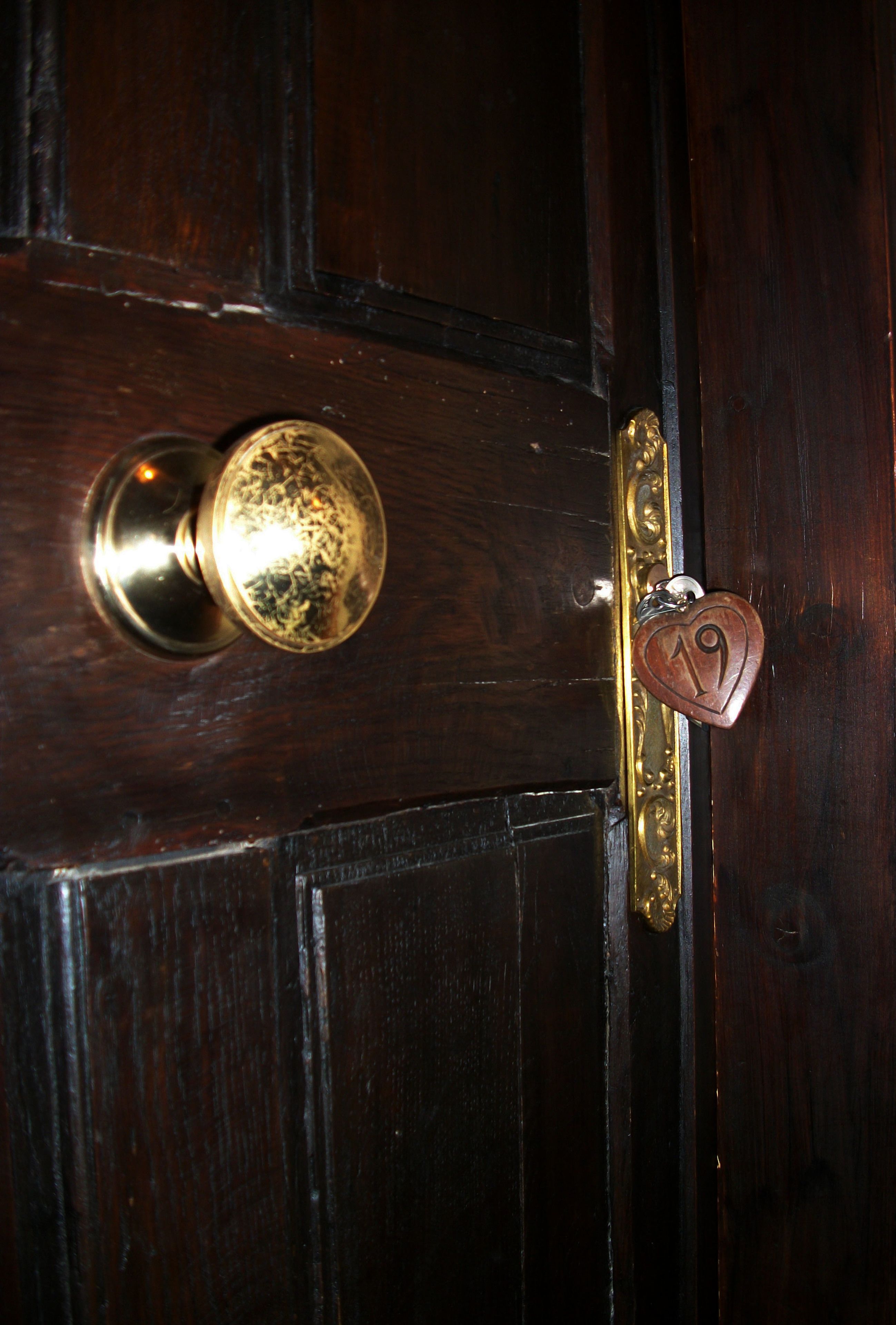 A wooden door with a brass doorknob and a heart-shaped keychain with the number 19.
