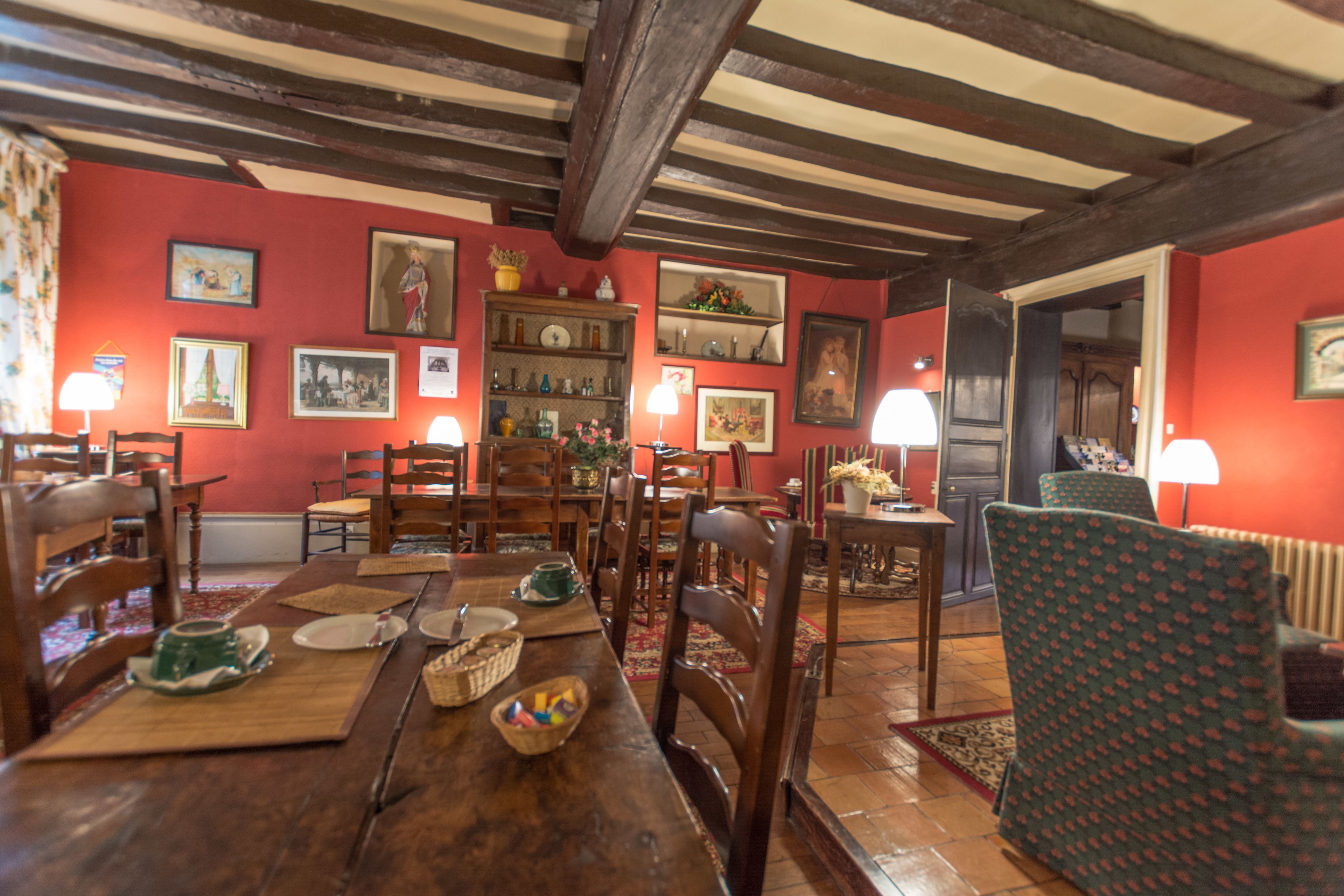 Un comedor con muebles de madera, una pared roja con cuadros enmarcados y techo de madera.