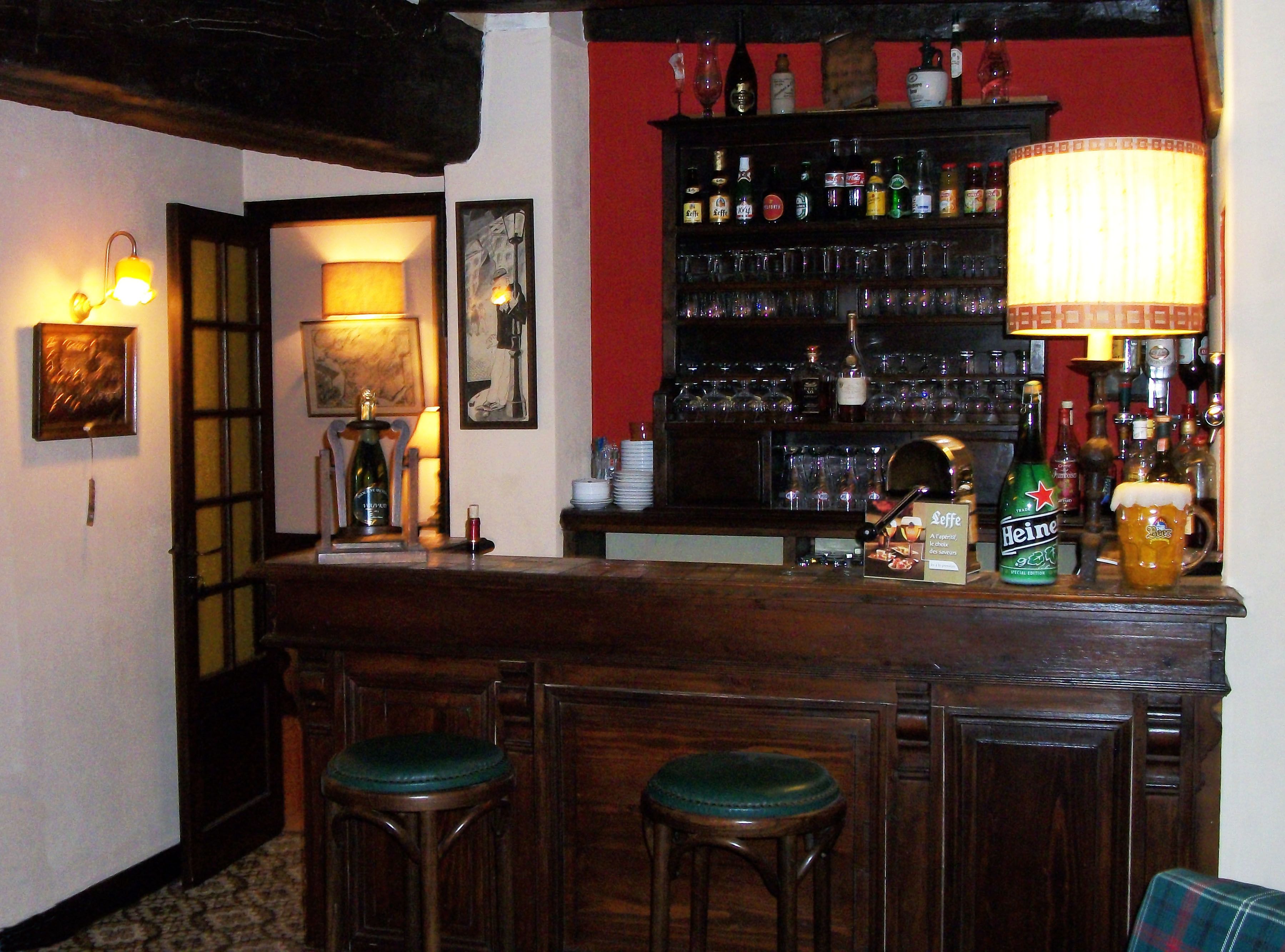 Una zona de bar con taburetes de madera, una estantería de licores y una lámpara.