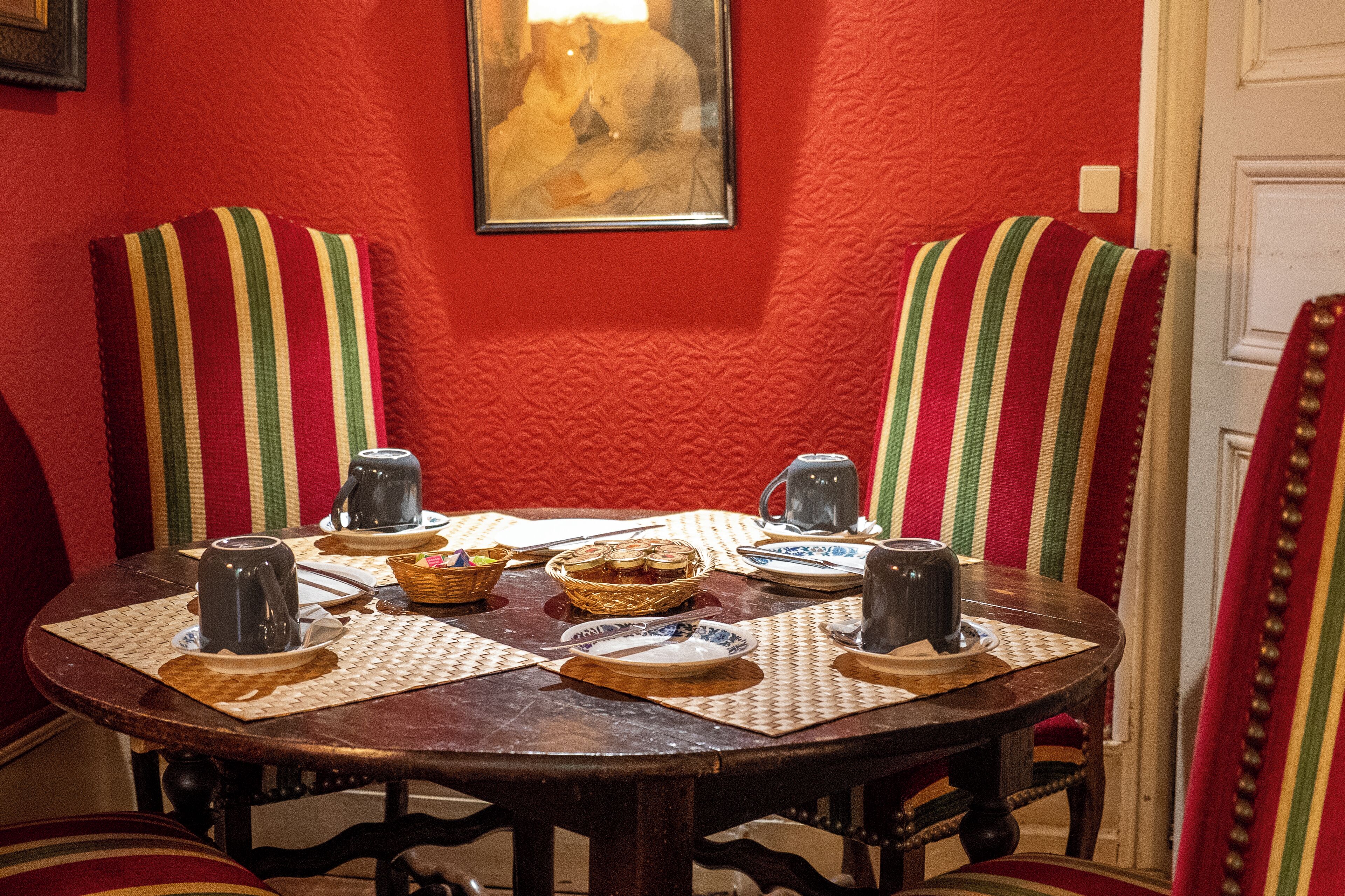 A dining table with placemats, a basket of bread, and two mugs.