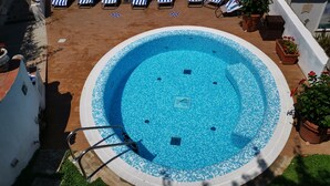Una piscina circular con borde de mosaicos, rodeada de sillas de descanso con cojines a rayas y plantas en macetas.
