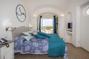 Un dormitorio con cama, teléfono en la mesita de noche, televisor de pared y balcón con vistas.