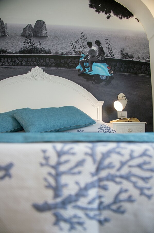 A bedroom with a bed, a nightstand, a lamp, and a wall mural of a couple on a scooter. - Villa Patrizi (Capri)