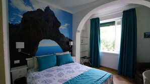 Un dormitorio con cama, mesita de noche, cómoda, ventana con cortinas y un mural en la pared.