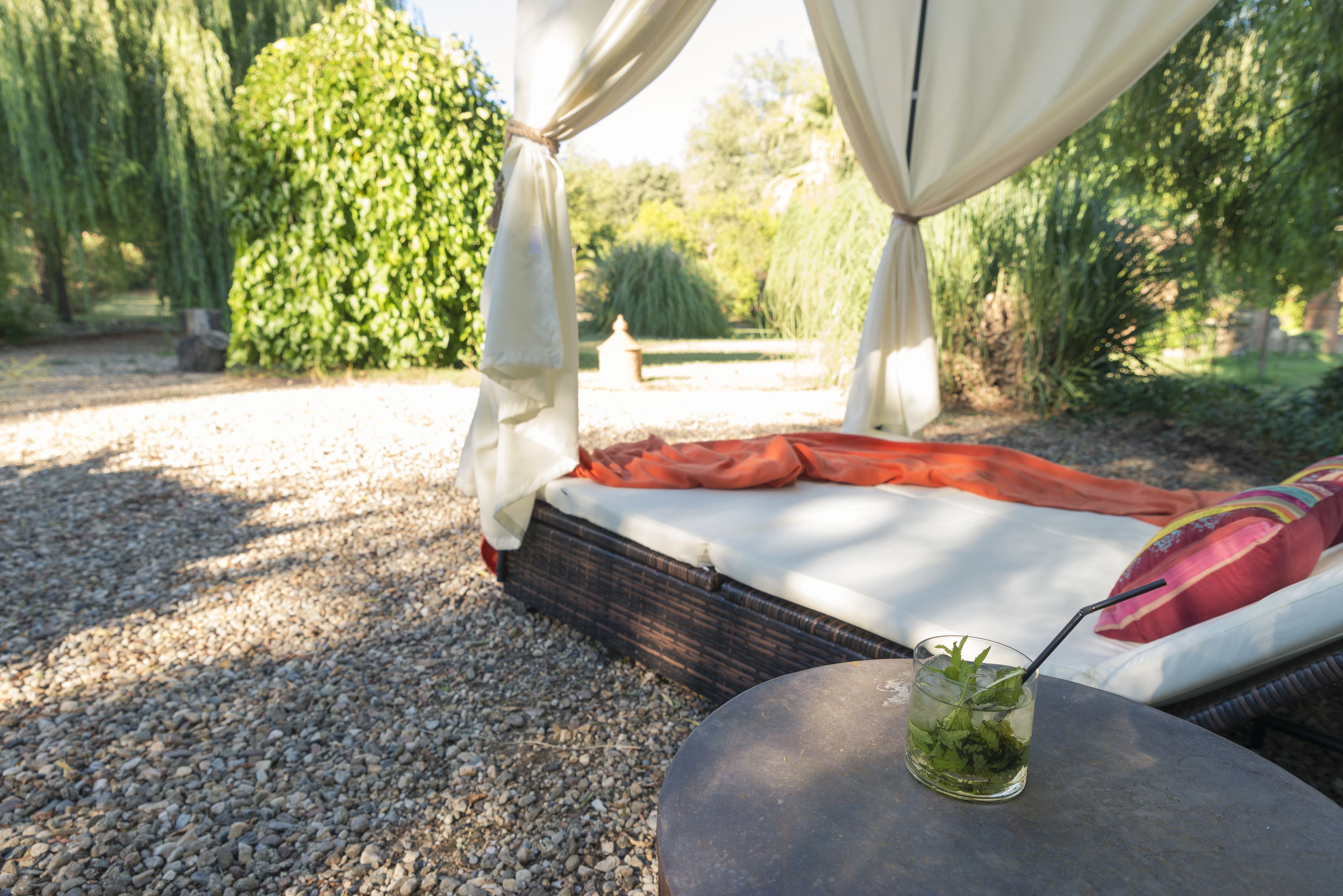 A bed with a white sheet and an orange blanket, a glass with a straw, and a table with a drink.