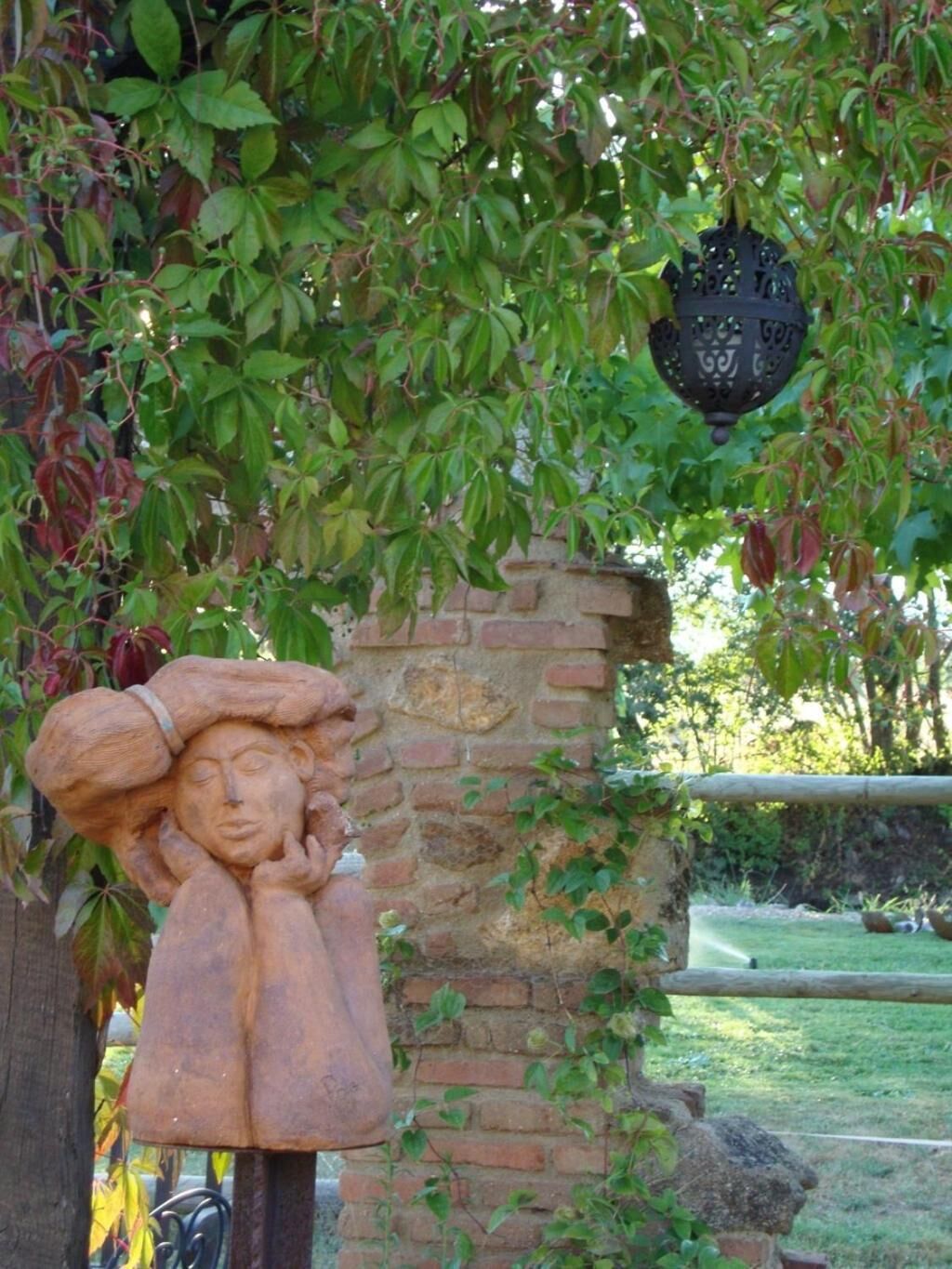 Un jardín con muro de ladrillo, una escultura de madera y un farol colgante.