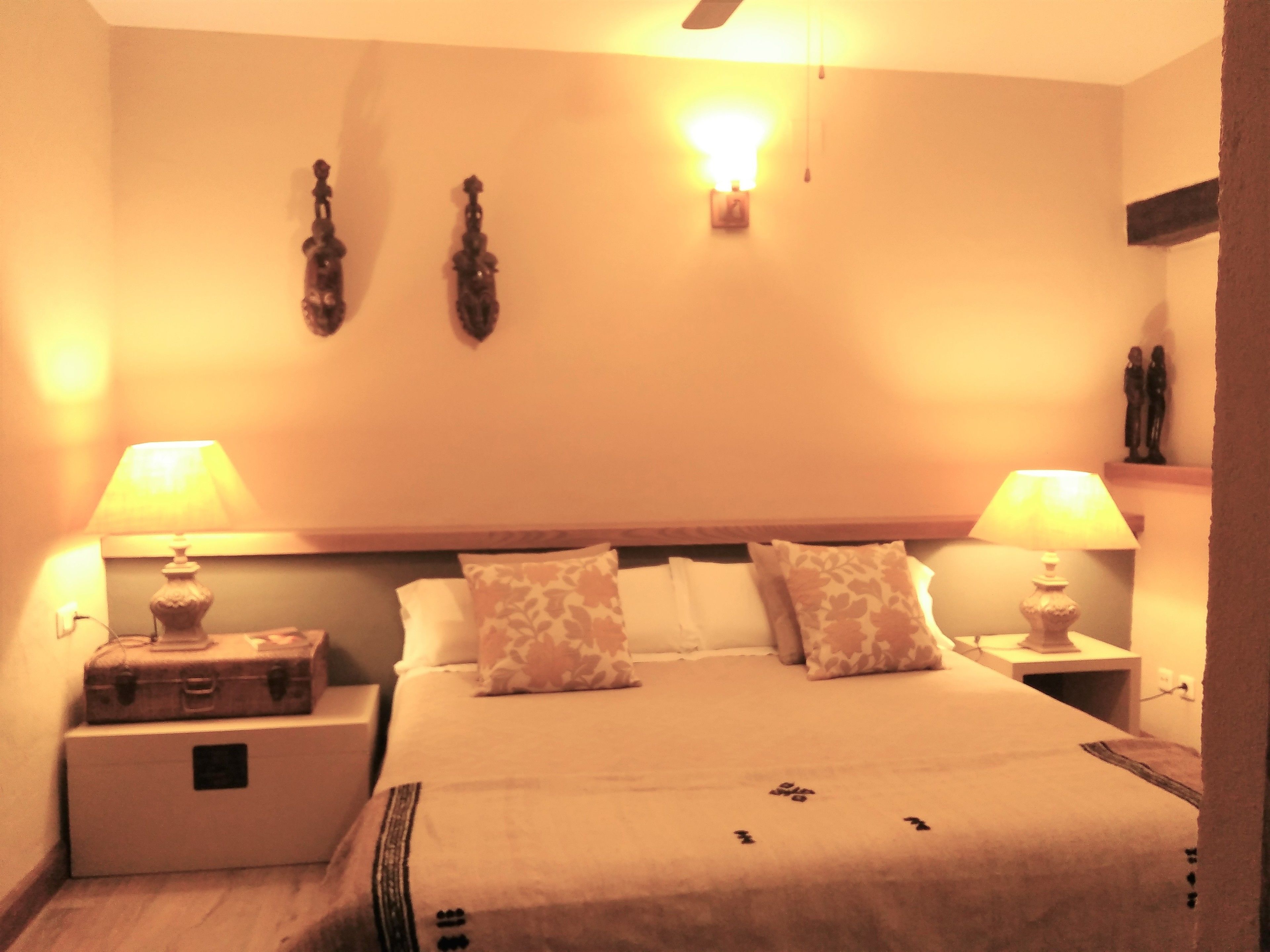 A hotel room with a bed, two bedside tables, a nightstand, a wall-mounted light, and a ceiling fan.