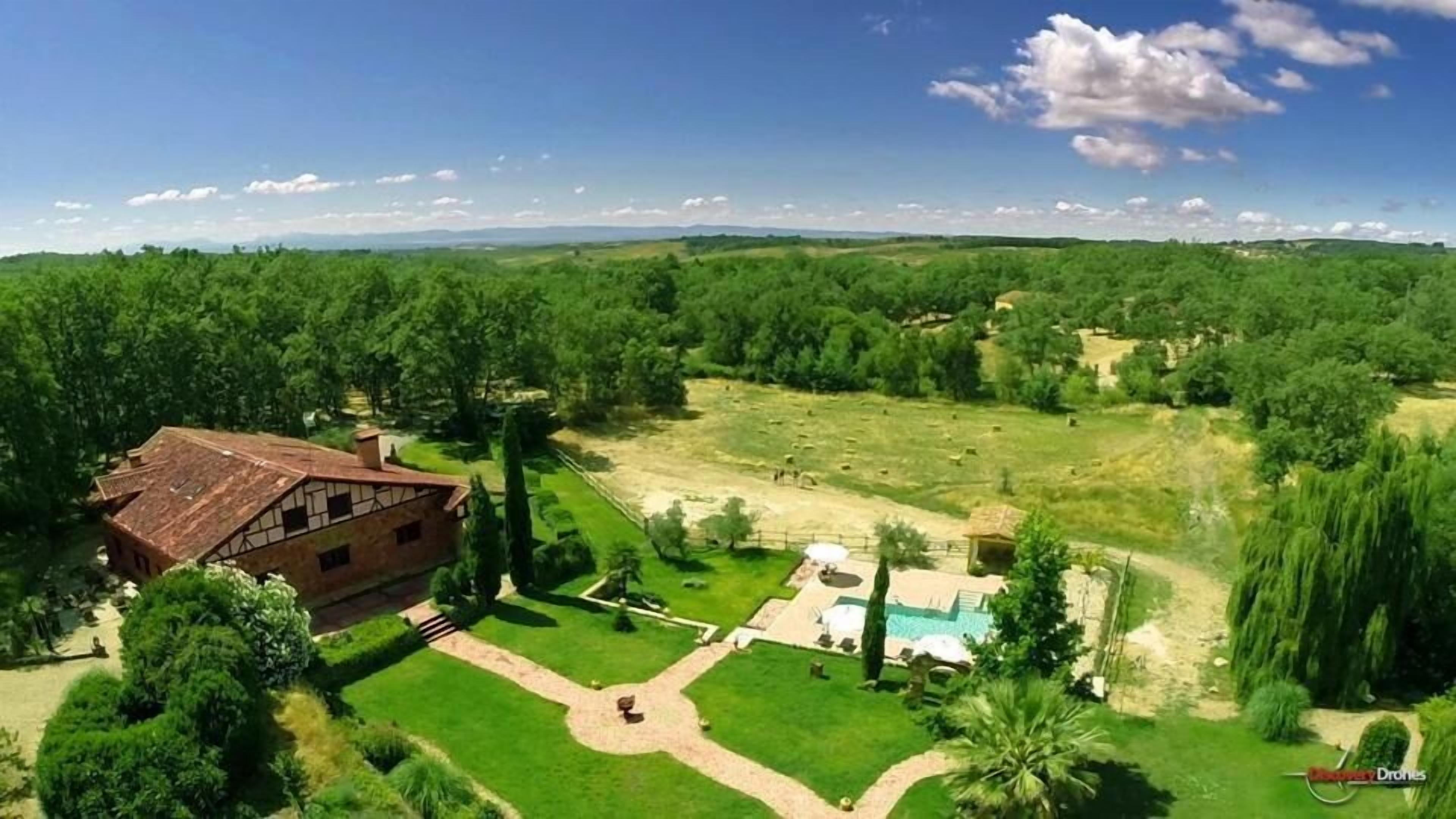 Vista aérea de una propiedad con una amplia casa de ladrillo, piscina y extensos campos verdes.