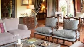 A spacious living room with a high ceiling, exposed wooden beams, and a large window with curtains. There are two sofas, a coffee table, and a side table with decorative items. - La Casona de Valfrío (Cuacos de Yuste)
