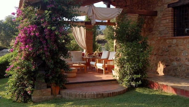 A stone building with a covered patio area featuring outdoor furniture and a pergola with draped fabric. - La Casona de Valfrío (Cuacos de Yuste)