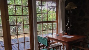A room with a wooden table and chairs, large windows with a view of trees, and a stone wall.