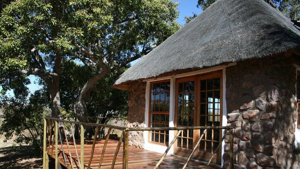 A thatched-roof hut with a wooden deck and stone walls.