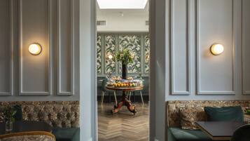 A hotel lobby with a central round table set for a meal, flanked by green upholstered seating and a patterned wall.