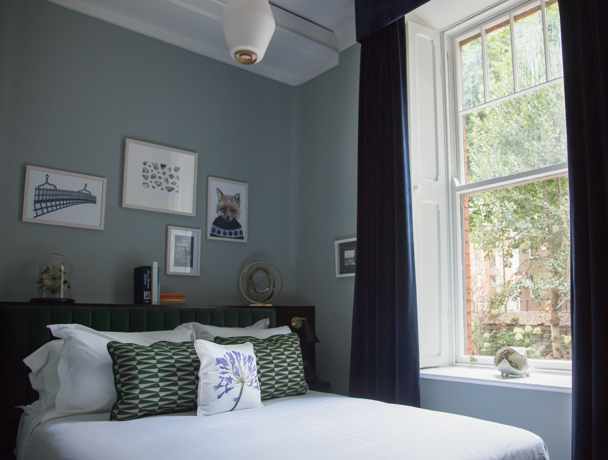 A bedroom with a bed, a window with curtains, and wall art including a fox and a bridge.