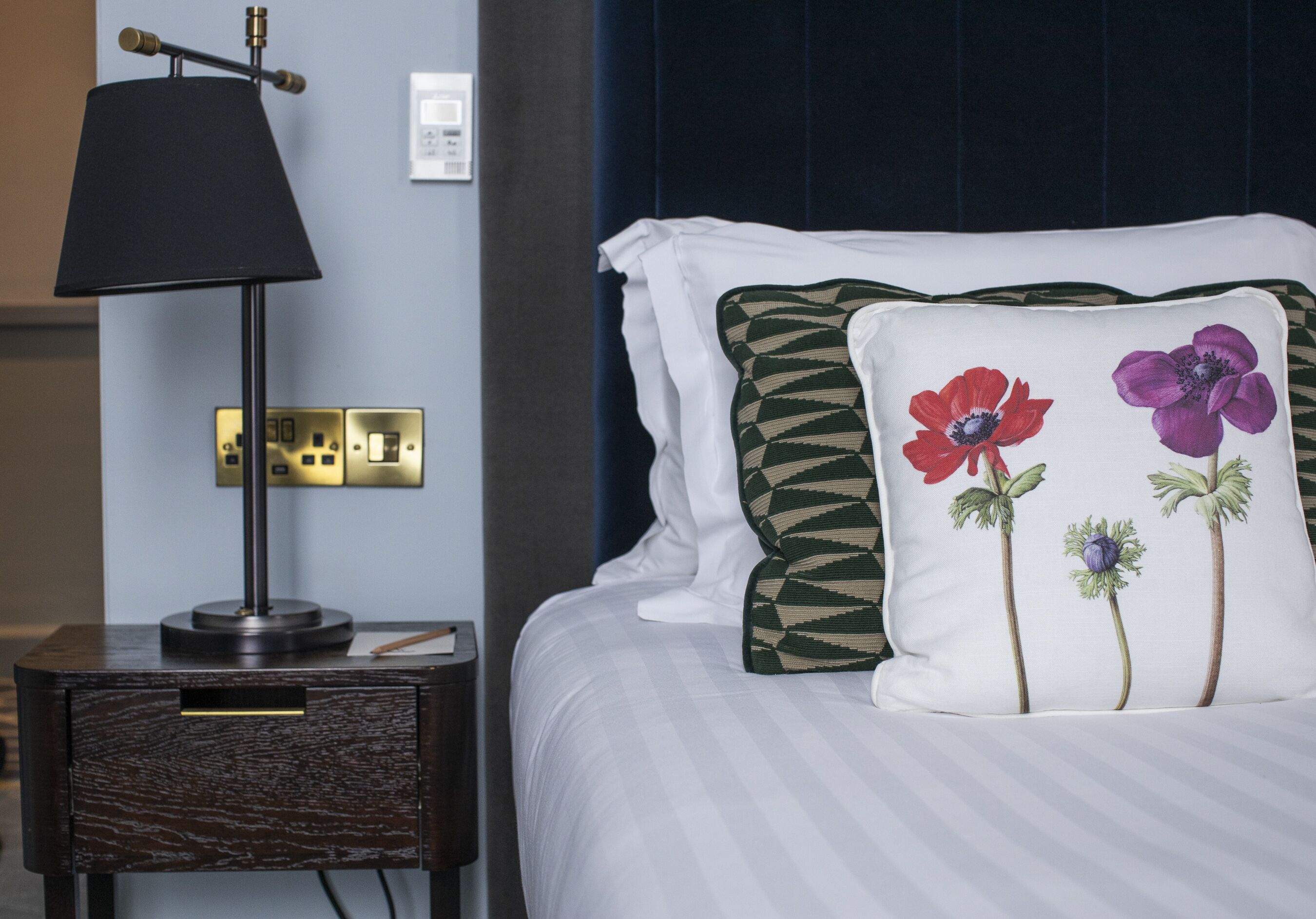 A neatly made bed with white bedding and decorative pillows featuring floral designs.