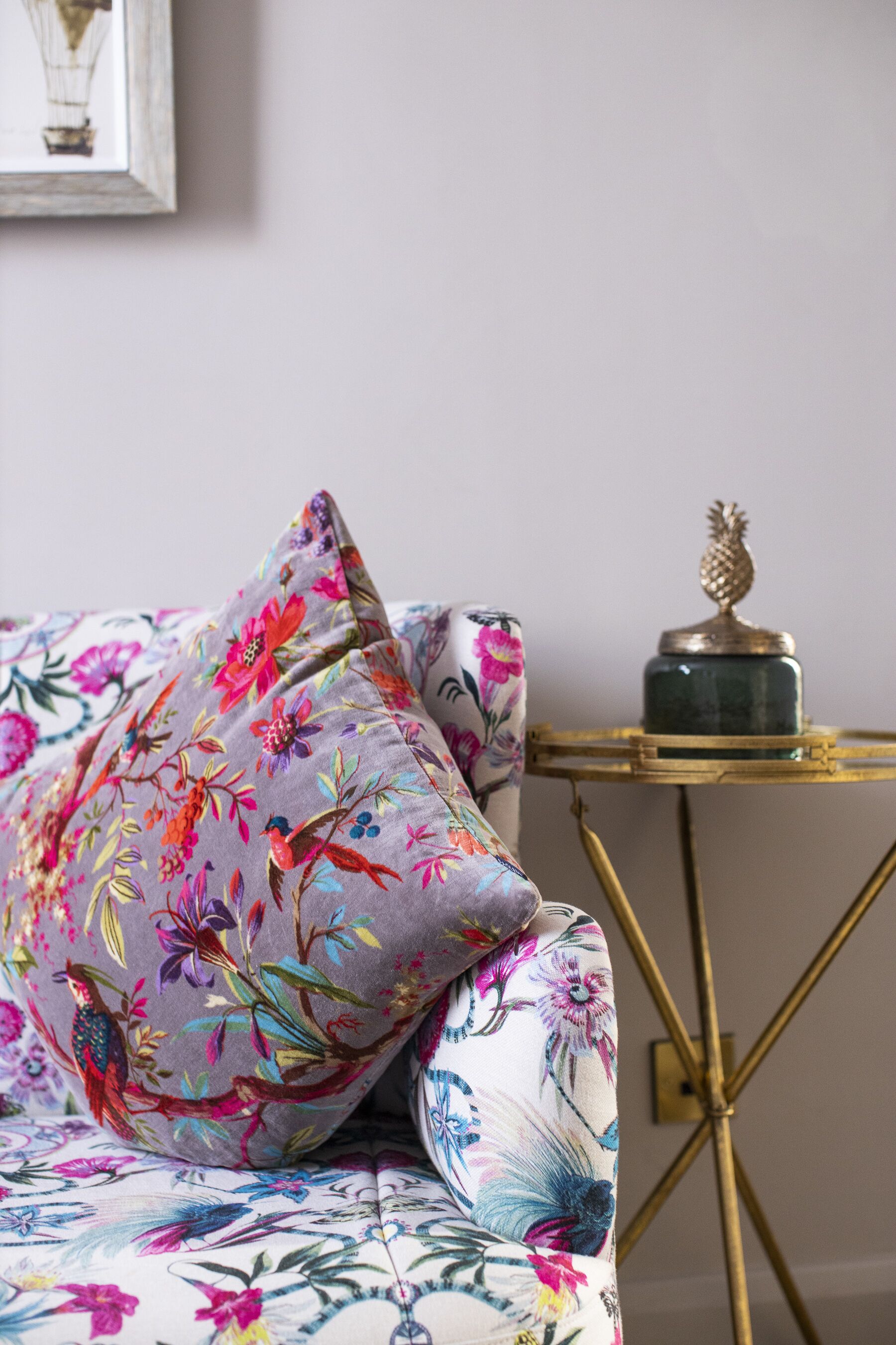 A bed with floral-patterned bedding, a small round table with a pineapple decoration, and a framed picture on the wall.