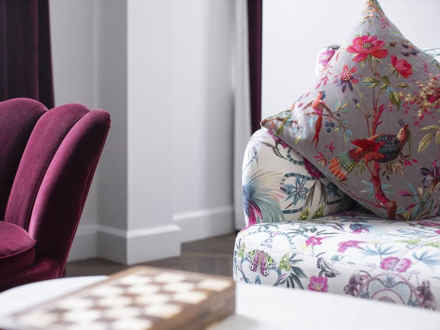 A plush purple armchair and a floral-patterned sofa in a well-lit room with a chessboard on a table.