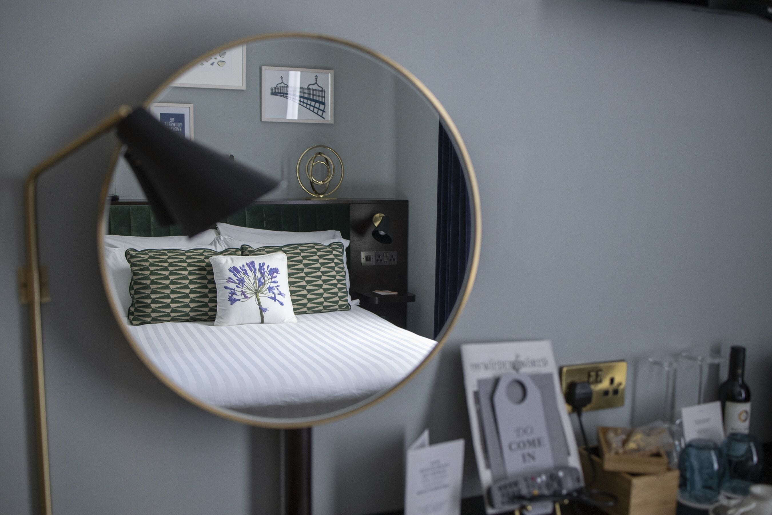 A bedroom with a bed, a round mirror, a bedside table, and a wall-mounted lamp.