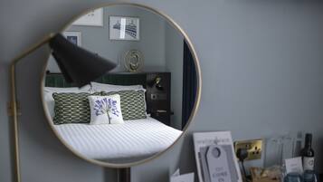 A bedroom with a bed, a round mirror, a bedside table, and a wall-mounted lamp.