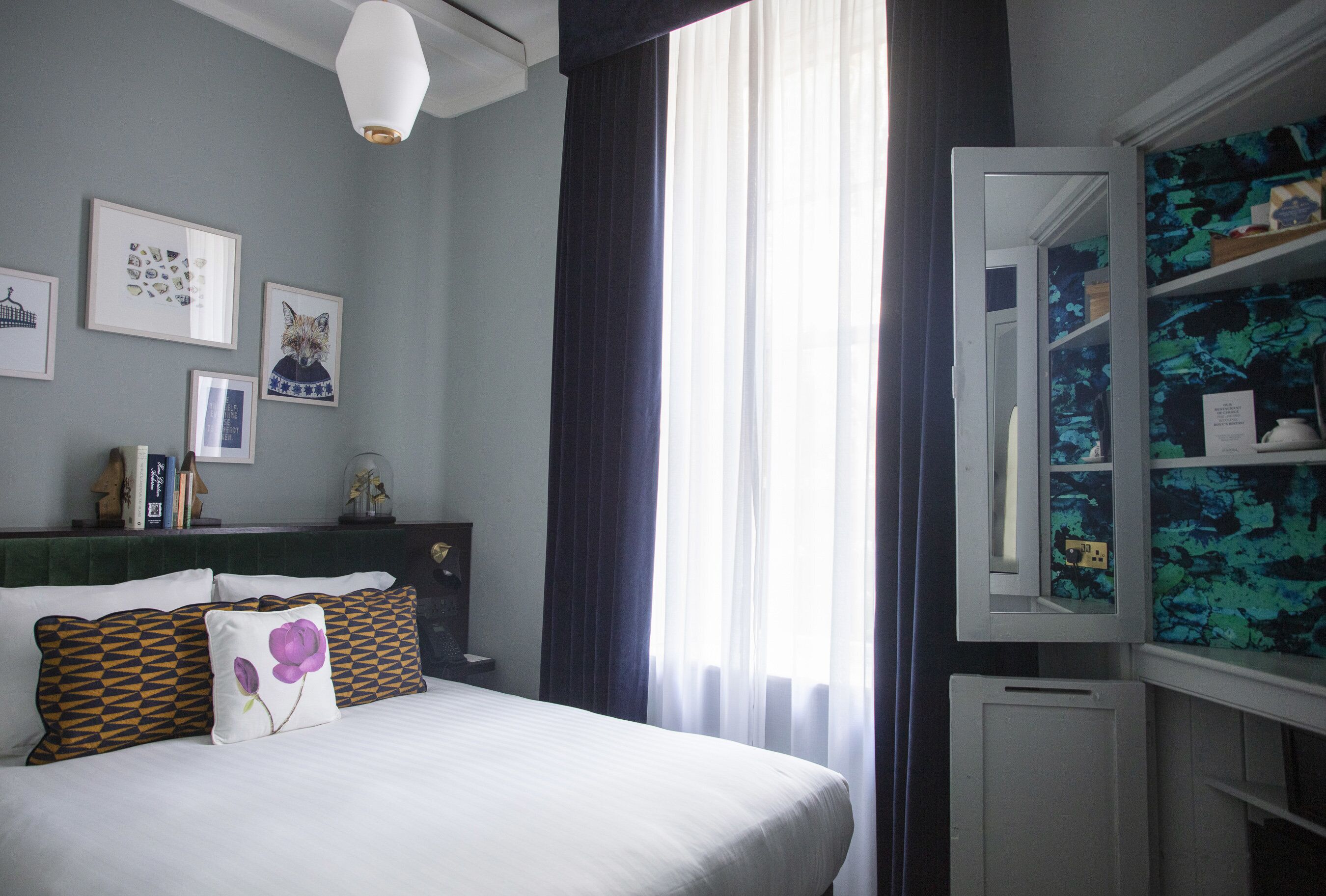 Une chambre à coucher avec un lit, des oreillers, une commode, un miroir et une fenêtre avec des rideaux.