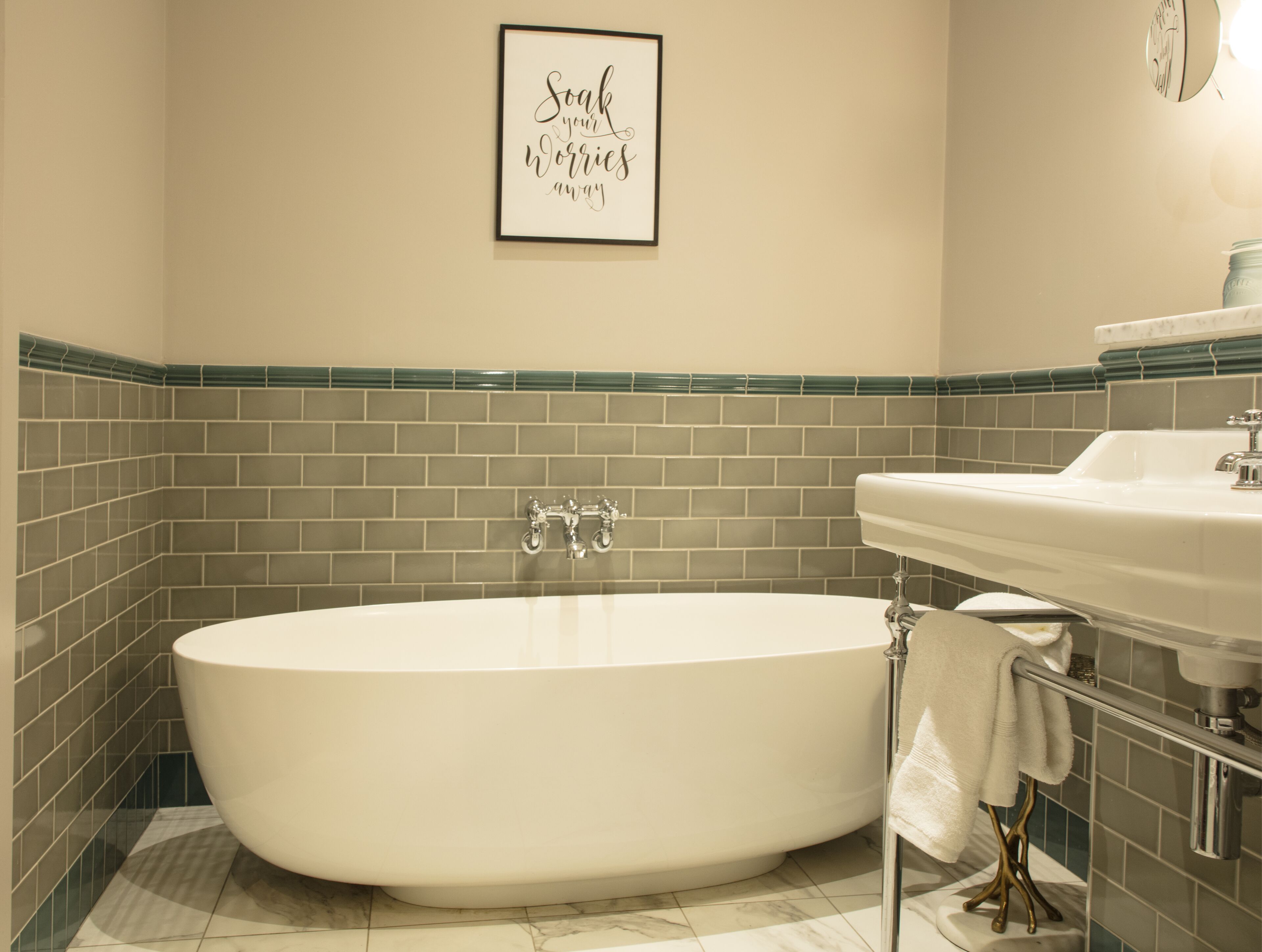 A bathroom with a freestanding bathtub, a sink, and a framed quote on the wall.