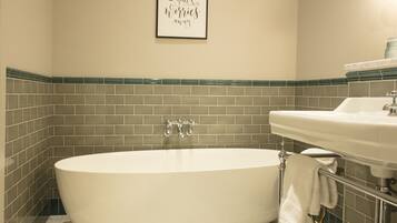 A bathroom with a freestanding bathtub, a sink, and a framed quote on the wall.