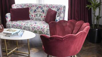 A room with a floral sofa, a red chair, a white coffee table, and a potted plant.