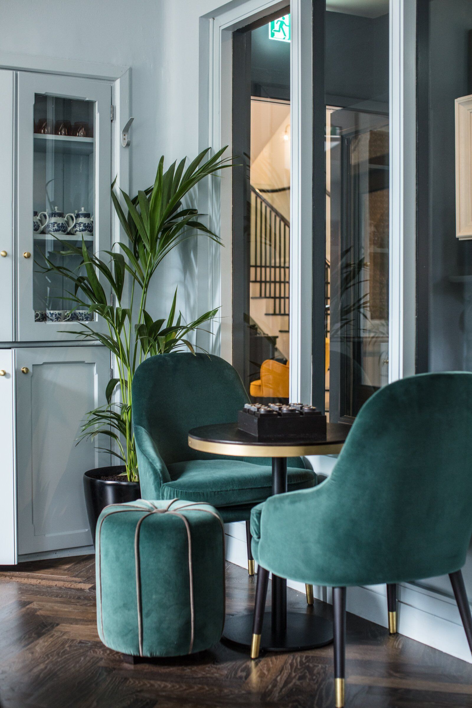 Een modern interieur met een groen bekleden stoel, een kleine ronde tafel en een potplant.