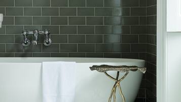 Un baño con una bañera independiente, una toalla al lado y un soporte metálico decorativo.