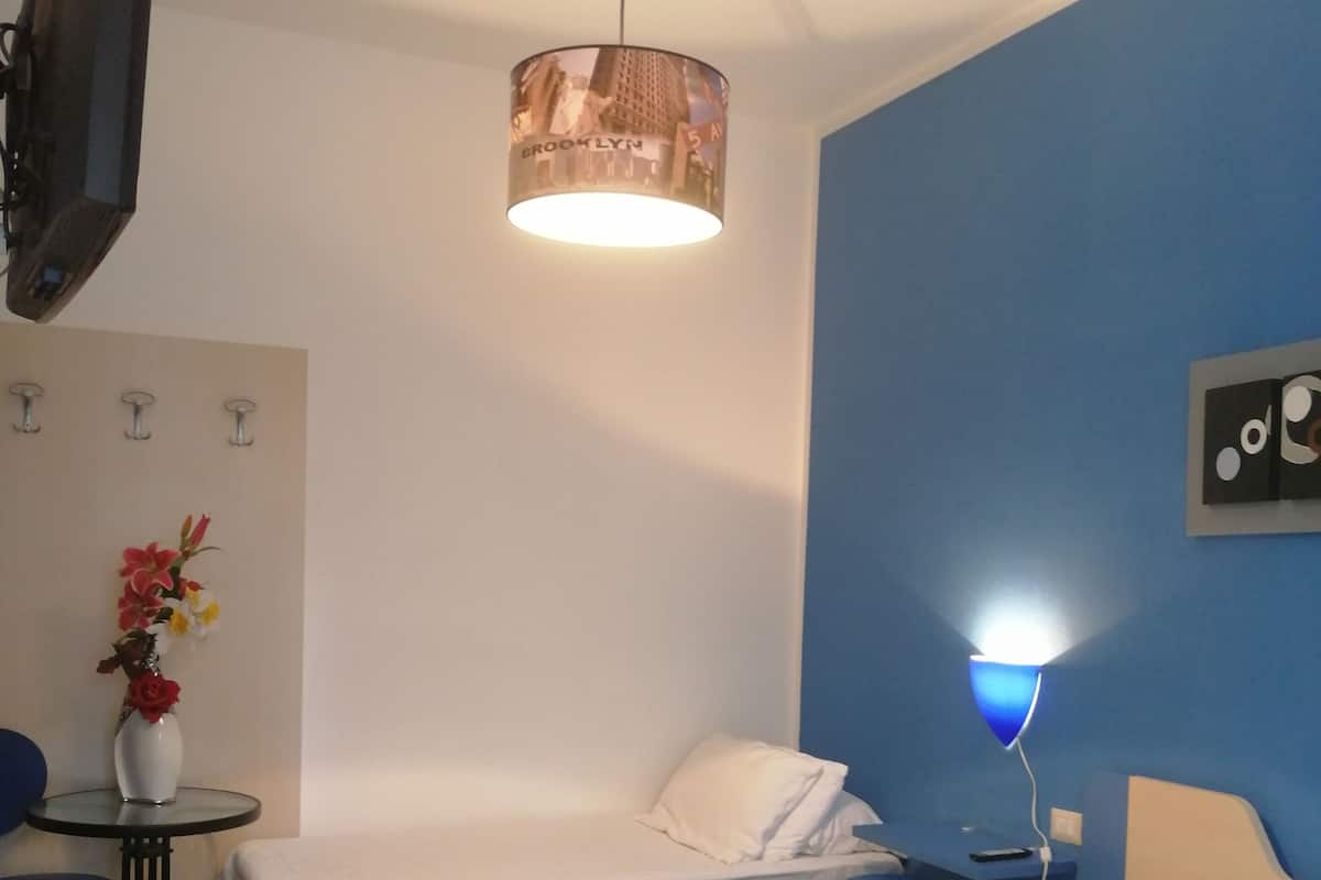 Habitación de hotel con dos camas, un escritorio, una silla, un televisor y una lámpara fijada a la pared.