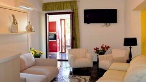 Una sala de estar con sofá, sillones, una mesa de centro, televisor y objetos decorativos, incluyendo un florero con flores rojas.