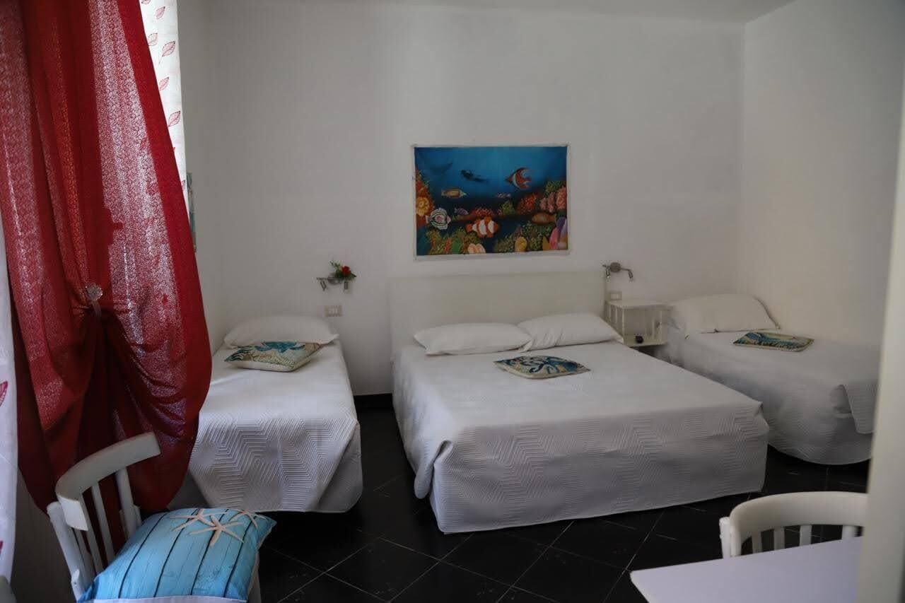 A room with three single beds, a painting of fish on the wall, and a red curtain.