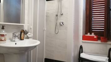 Un baño con lavamanos, espejo, ducha y ventana con persianas.