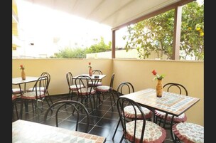 Una terrazza esterna con pavimento piastrellato, tavoli rotondi con cuscini fiorati e sedie.