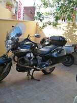 Una motocicletta parcheggiata su una superficie piastrellata, con un muro giallo e piante in vaso sullo sfondo.