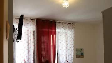 A small, dimly lit room with a single bed, a small table with a chair, and a TV mounted on the wall.