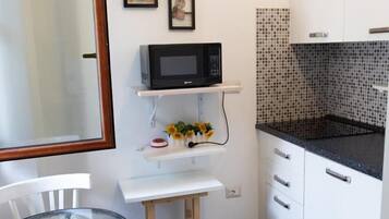 A compact kitchen with white cabinets, a black countertop, a microwave, and a small table with a chair.