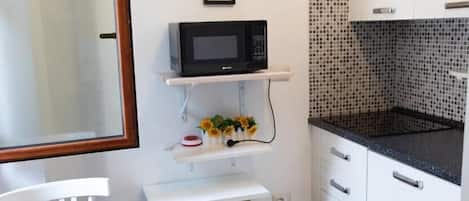A compact kitchen with white cabinets, a black countertop, a microwave, and a small table with a chair.