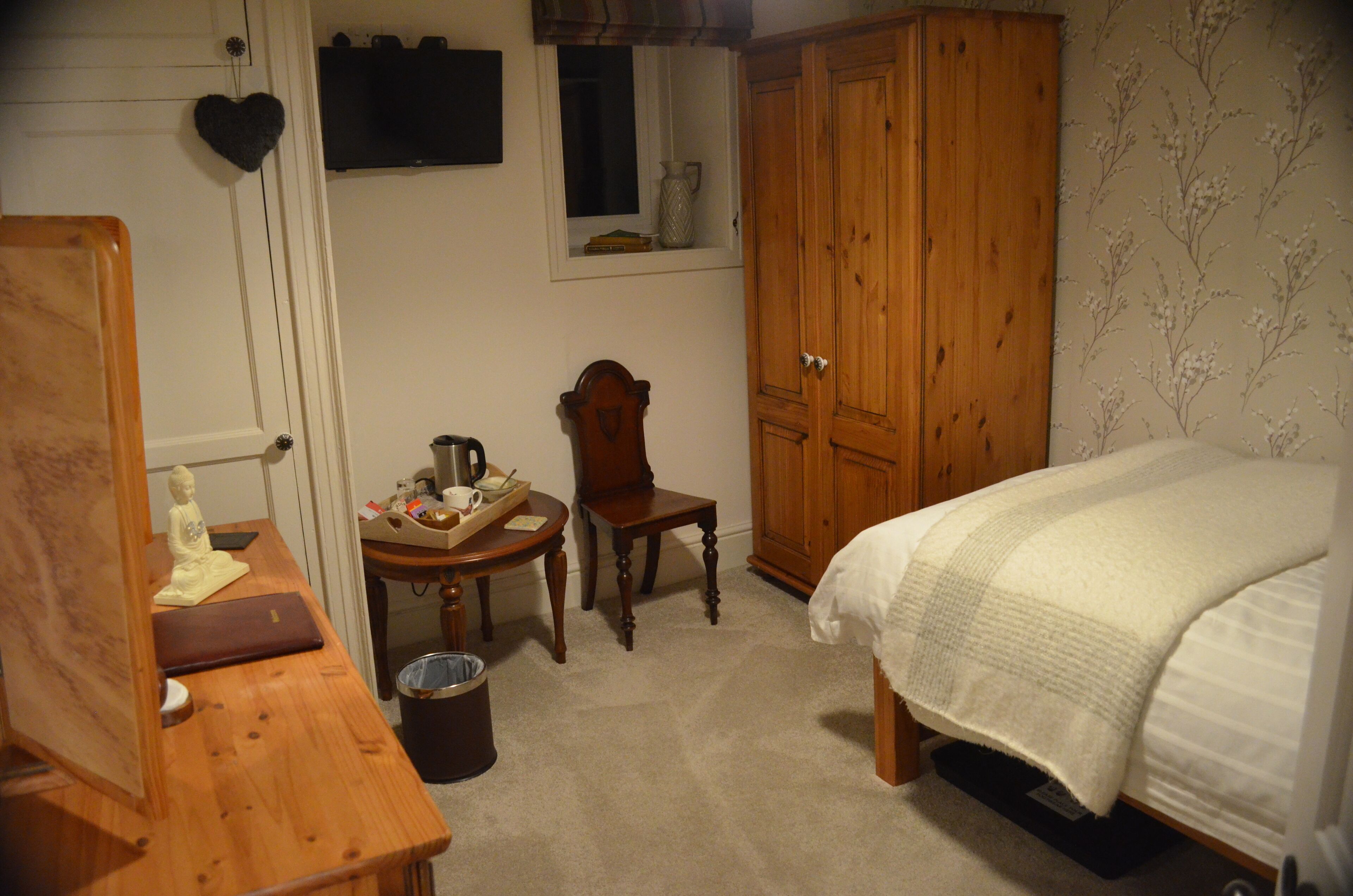 Une chambre à coucher avec un lit, une armoire en bois, un bureau avec une chaise et une petite fenêtre.