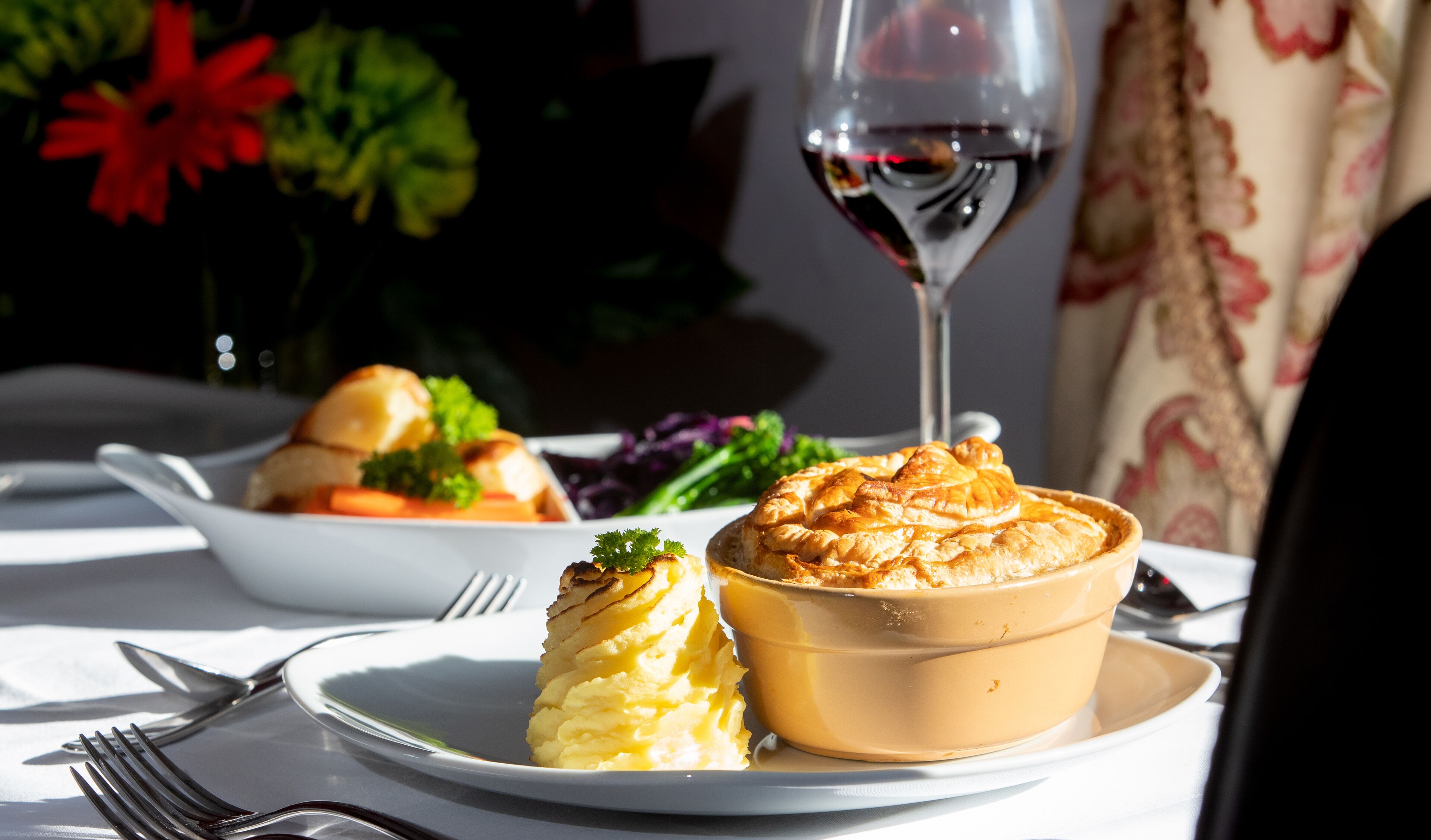 Ein Esstisch mit einem Teller Essen, einem Glas Rotwein und einer Schüssel Suppe.