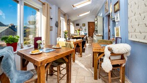 A cozy dining area with wooden tables and chairs, a view of the sky through large windows, and a blue wall with framed pictures. - Middle Studfold Farm B&B (Settle)