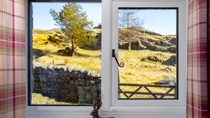 A window with a view of a stone wall and a wooden fence, a metal sculpture of a rabbit, and a plaid curtain. - Middle Studfold Farm B&B (Settle)