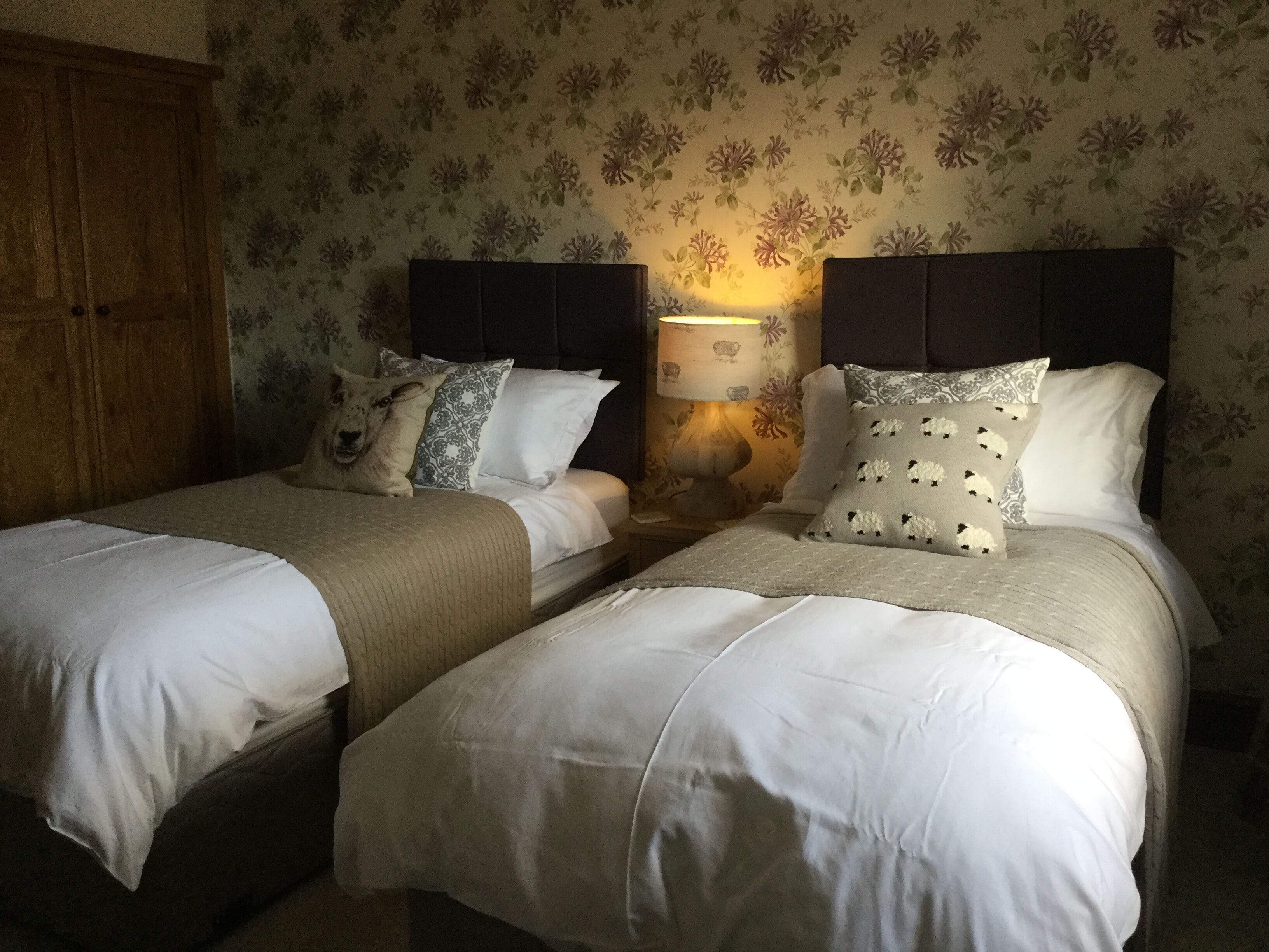 A room with two beds, a wooden wardrobe, and floral wallpaper.