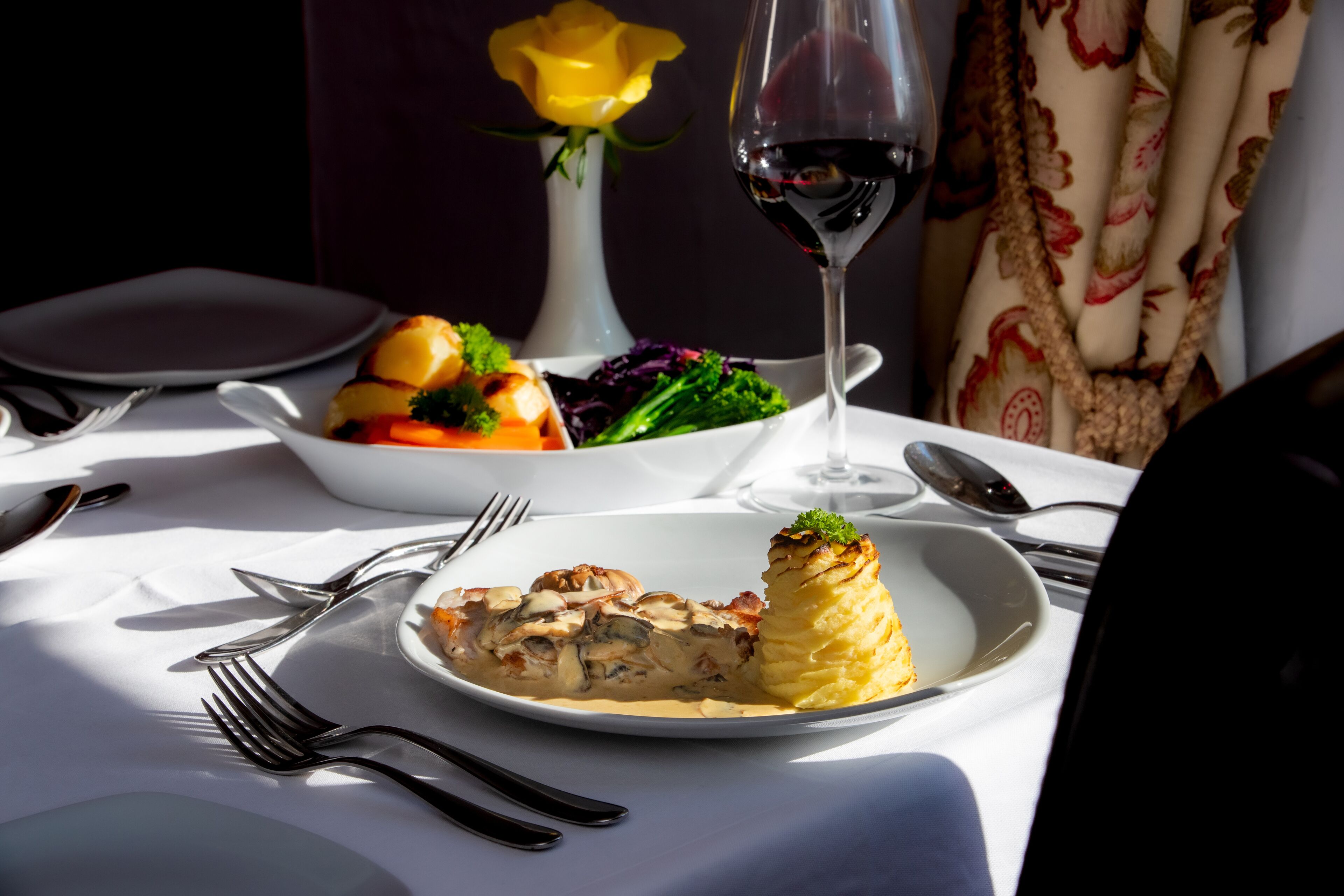A dining table with plates of food, a wine glass, and cutlery.