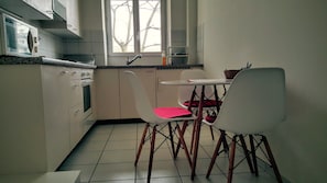 A compact kitchen with white cabinets, a microwave, and a small dining table with two chairs. - Basel Charme Apartments (Basel)