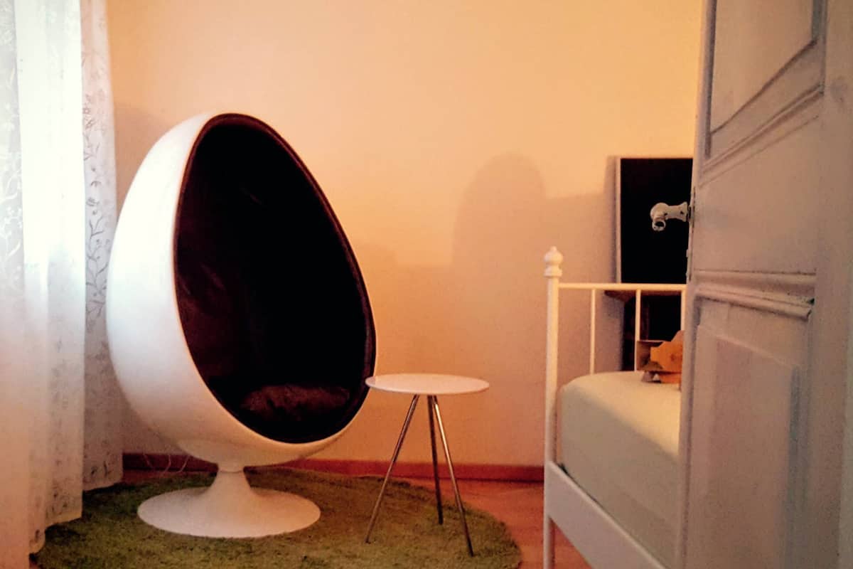 A room with a unique egg-shaped chair, a small white table, and a bed with a white headboard.