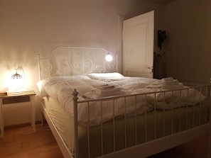 A neatly made bed with white linens and towels, a bedside table with a lamp, and a door with a light switch. - Basel Charme Apartments (Basel)