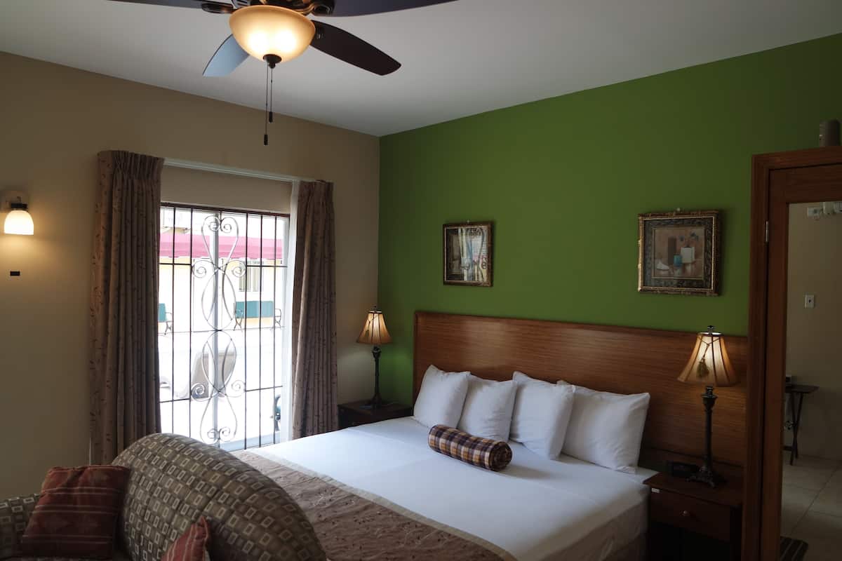 A hotel room with a bed, two bedside lamps, a ceiling fan, a window with curtains, and two framed pictures on the wall.
