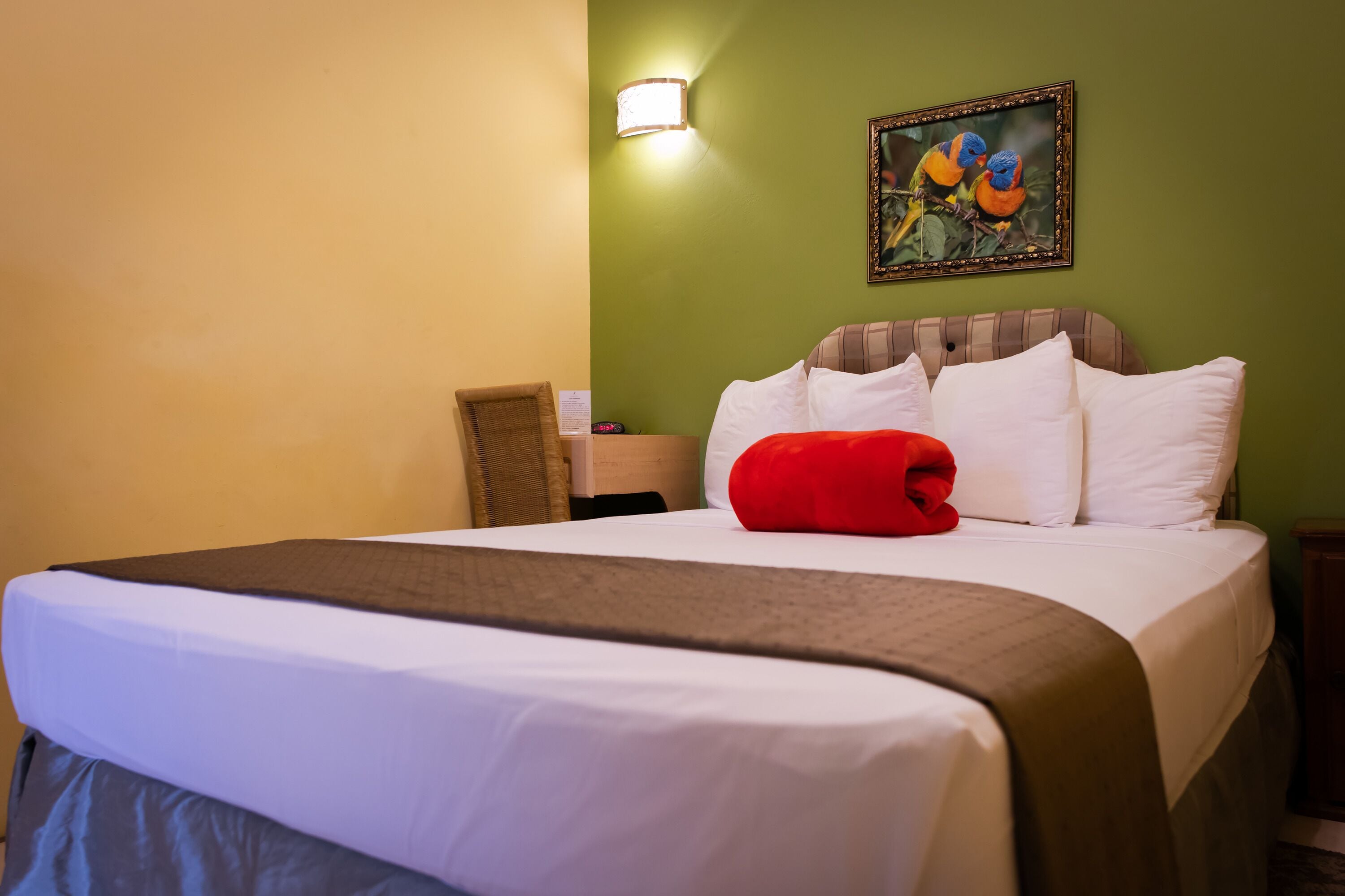 A hotel room with a bed, a nightstand, a lamp, and a painting of birds on the wall.