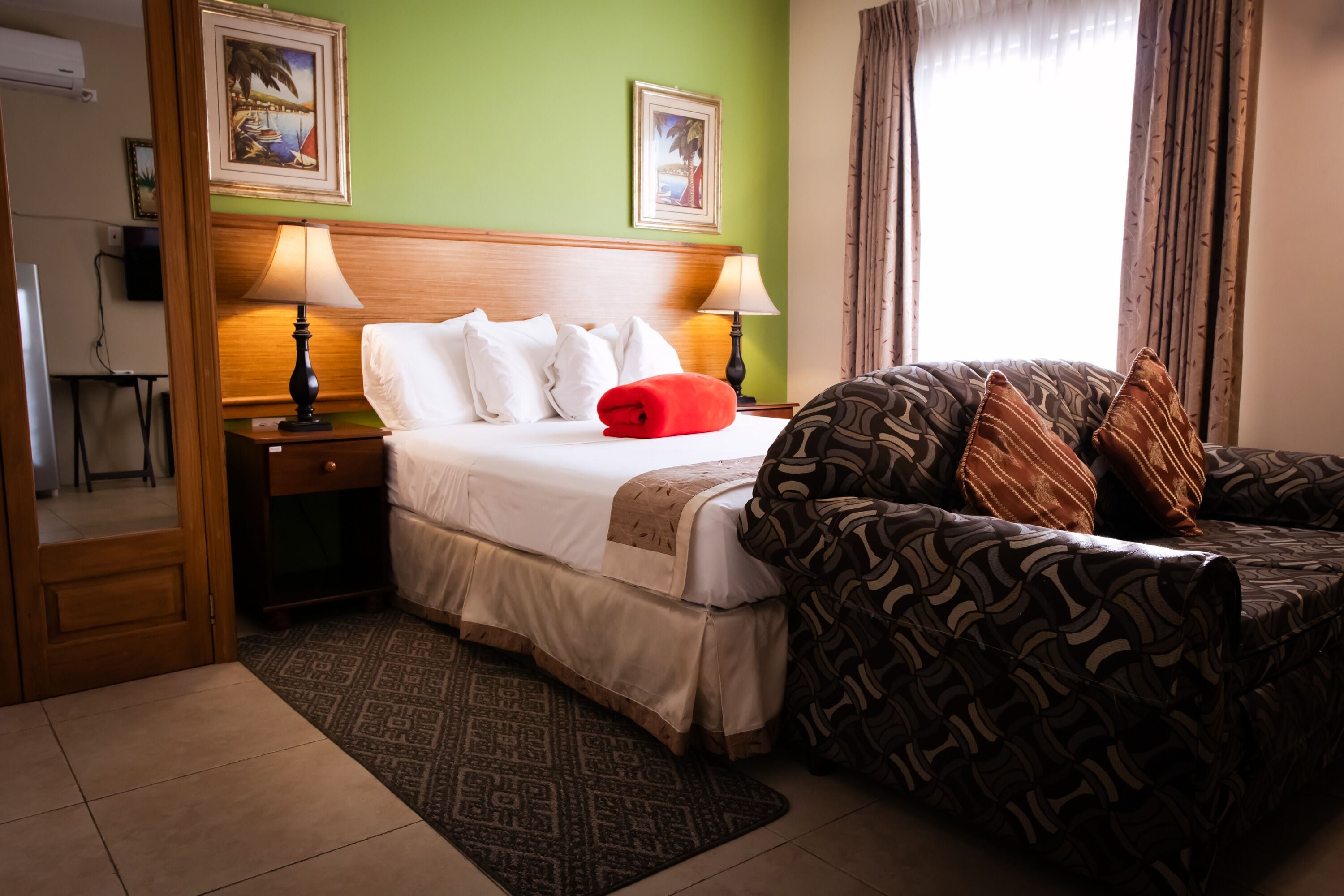 A hotel room with a bed, a sofa, two lamps, a patterned rug, and two framed pictures on the wall.